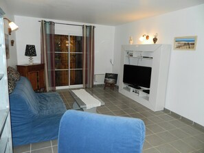Una sala de estar con un sofá, una televisión y un ventanal corredero.