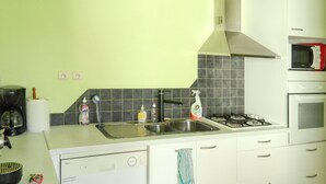 A modern kitchen with white cabinets, a stainless steel sink, a gas stove, and a microwave. - Homerez - House Le Verdon + Private Garden (Le Verdon-sur-Mer)