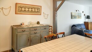 A dining area with a checkered tablecloth, wooden chairs, a cabinet with decorative items, and a blue sofa. - Homerez - House Le Verdon + Private Garden (Le Verdon-sur-Mer)