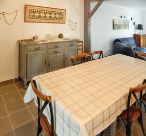 Un comedor con mantel de cuadros, sillas de madera, un aparador con adornos y un sofá azul.