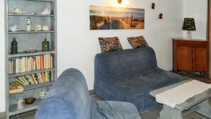 A living room with two blue sofas, a bookshelf, a painting, and a small cabinet. - Homerez - House Le Verdon + Private Garden (Le Verdon-sur-Mer)
