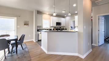 Une cuisine moderne avec des meubles blancs, un îlot central, des luminaires suspendus et un coin repas comprenant une table et des chaises.