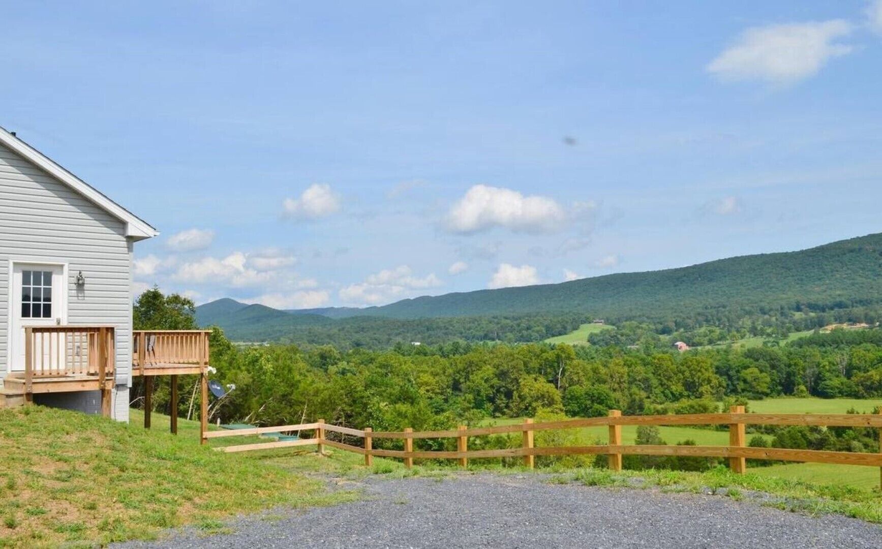 A house with a deck and a view of a green landscape and hills.