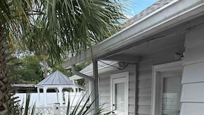 A covered patio with a table and chairs, a white building, and a palm tree. - 8th Green Cottage "A relaxing Oasis in the city" Guesthouse (Orlando)