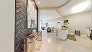 Eine moderne Küche mit einer zentralen Kochinsel, einem Essbereich mit Stühlen und einem Flur mit Zierfischgrätmuster an der Wand und einem gerahmten Bild.