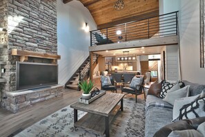 A spacious living area with a stone fireplace, a flat-screen TV, a wooden coffee table, and a cozy seating arrangement.
