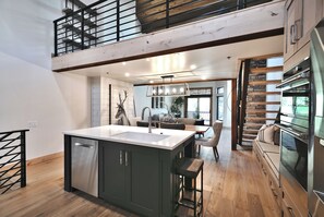 A spacious kitchen with a central island, a dining area with a bench, and a staircase leading to an upper level.
