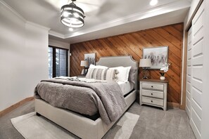 Un dormitorio con cama, mesitas de noche, lámpara, un cuadro y pared de madera.