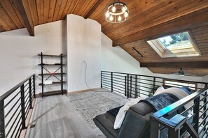 A loft bedroom with a sloped ceiling, a skylight, a staircase, and a bed with a headboard.