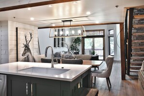 Eine moderne Küche mit einer zentralen Kochinsel, ein Essbereich mit Tisch und Stühlen sowie ein Wohnbereich mit Sofa und Kamin.