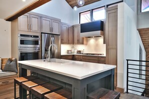 Una cocina moderna con electrodomésticos integrados, una isla grande y una zona de comedor con mesas de madera.