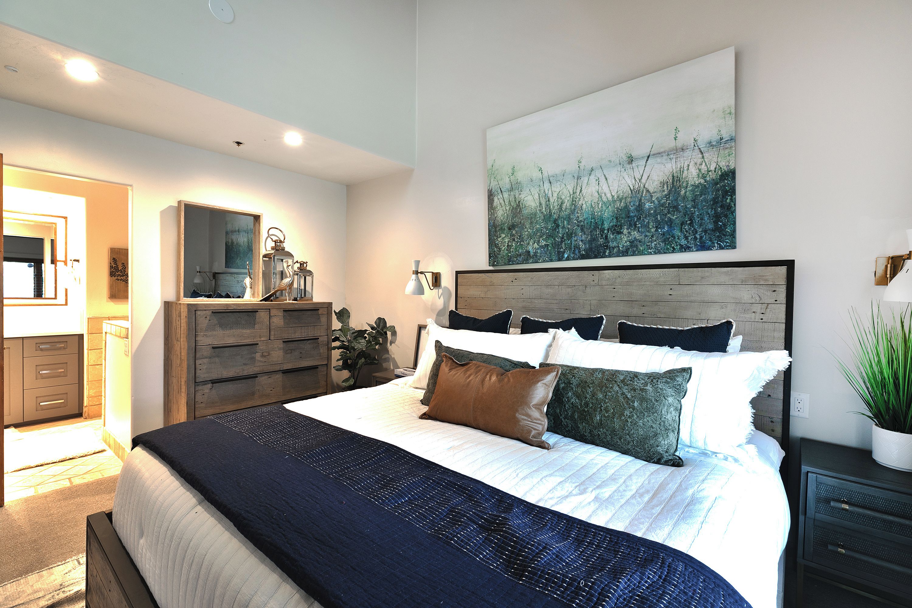 Een moderne slaapkamer met een groot bed, een houten hoofdbord, een kunstwerk aan de muur en een nachtkastje met een lamp.
