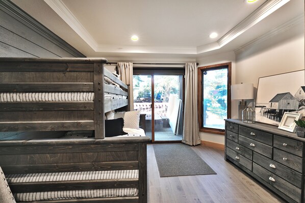 A room with a bunk bed, a dresser, and a large window.