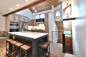 A modern kitchen with wooden cabinets, a large island with bar stools, stainless steel appliances, and a view of the outdoors through a window.