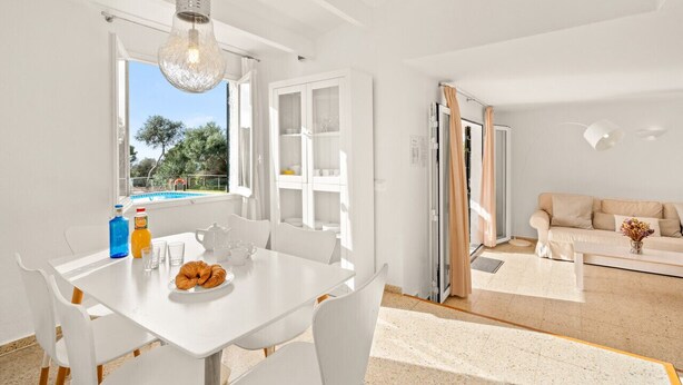 A bright, white interior with a dining area, a sofa, and a view of the outdoors.