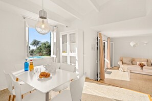 Un interior luminoso y blanco con comedor, sofá y vistas al exterior.