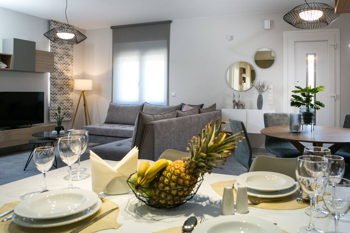 Una sala de estar moderna con comedor, televisor y un ventanal grande.