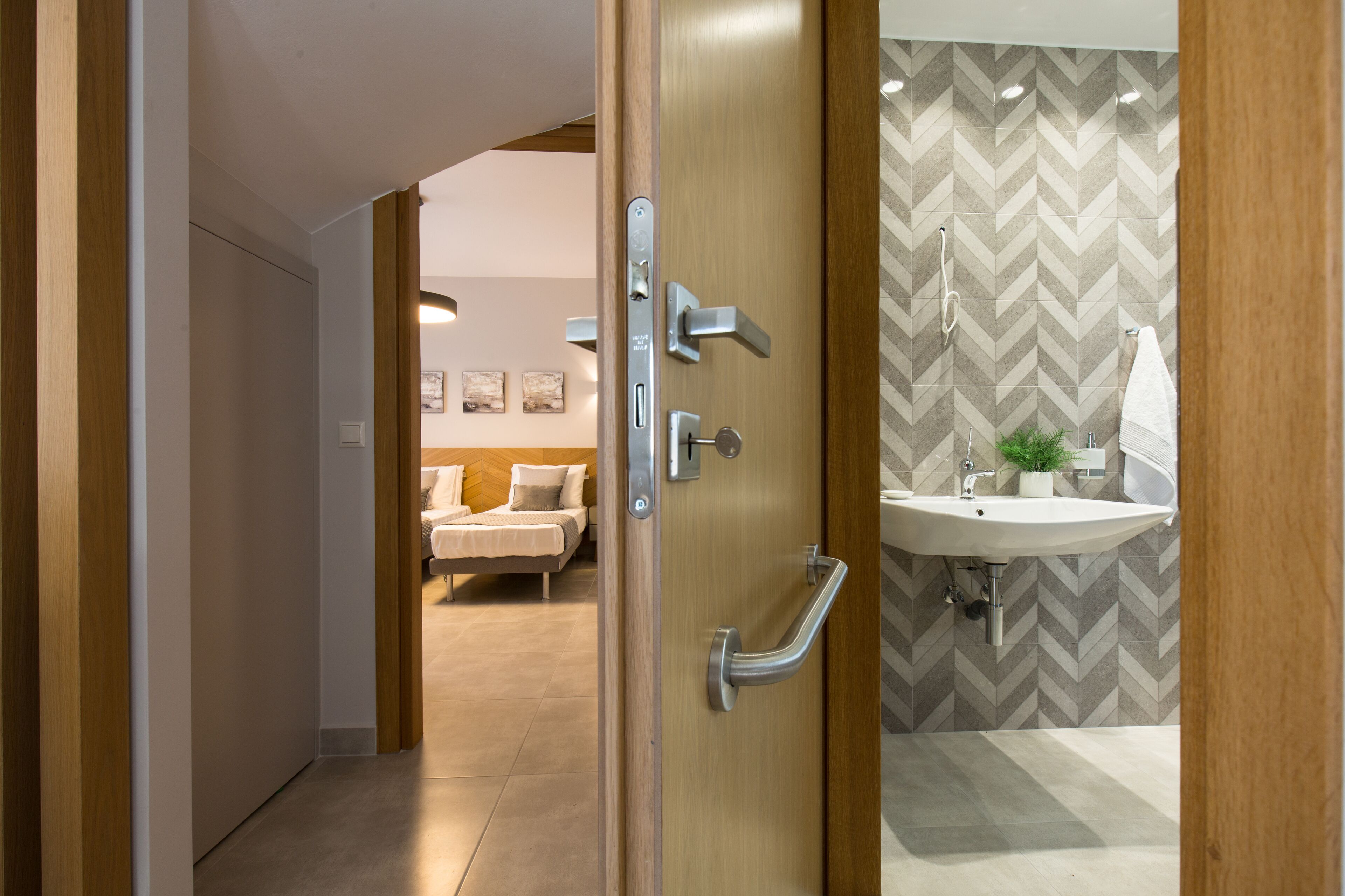 Une salle de bain moderne avec une porte en bois, un lavabo et un mur orné d’un motif en chevrons.