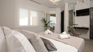 A modern hotel room with a large bed, a desk, a TV, and a balcony view.