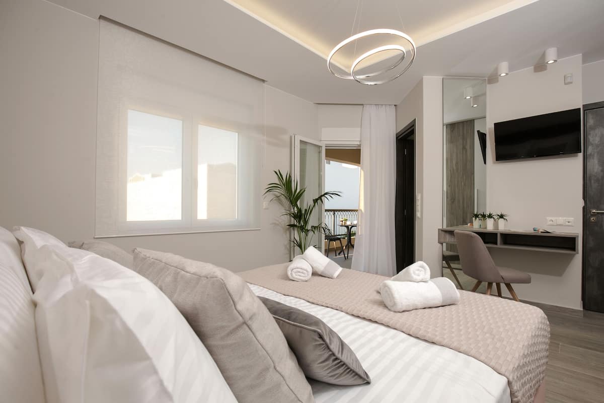 Habitación de hotel moderna con una cama grande, un escritorio, un televisor y vistas al balcón.