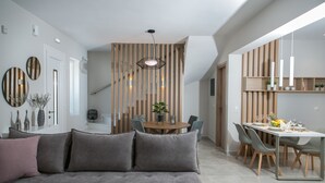 A modern living room with a grey sofa, a dining area with a wooden table and chairs, and a kitchen area with pendant lights.