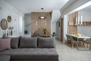 A modern living room with a grey sofa, a dining area with a wooden table and chairs, and a kitchen area with pendant lights.