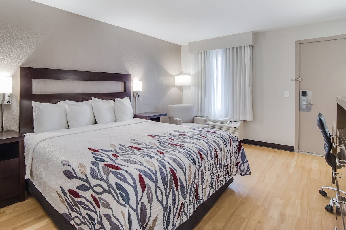 Ein Hotelzimmer mit einem großen Bett, einem Schreibtisch, einem Sessel, einer Lampe und einem Fenster mit Vorhängen.