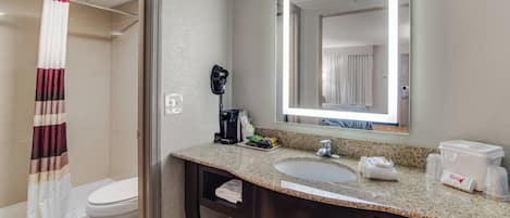 A hotel bathroom with a shower, toilet, sink, and a coffee machine.