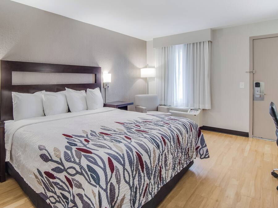 A hotel room with a large bed, bedside tables, a desk, a chair, a window with curtains, and a door with a lock.