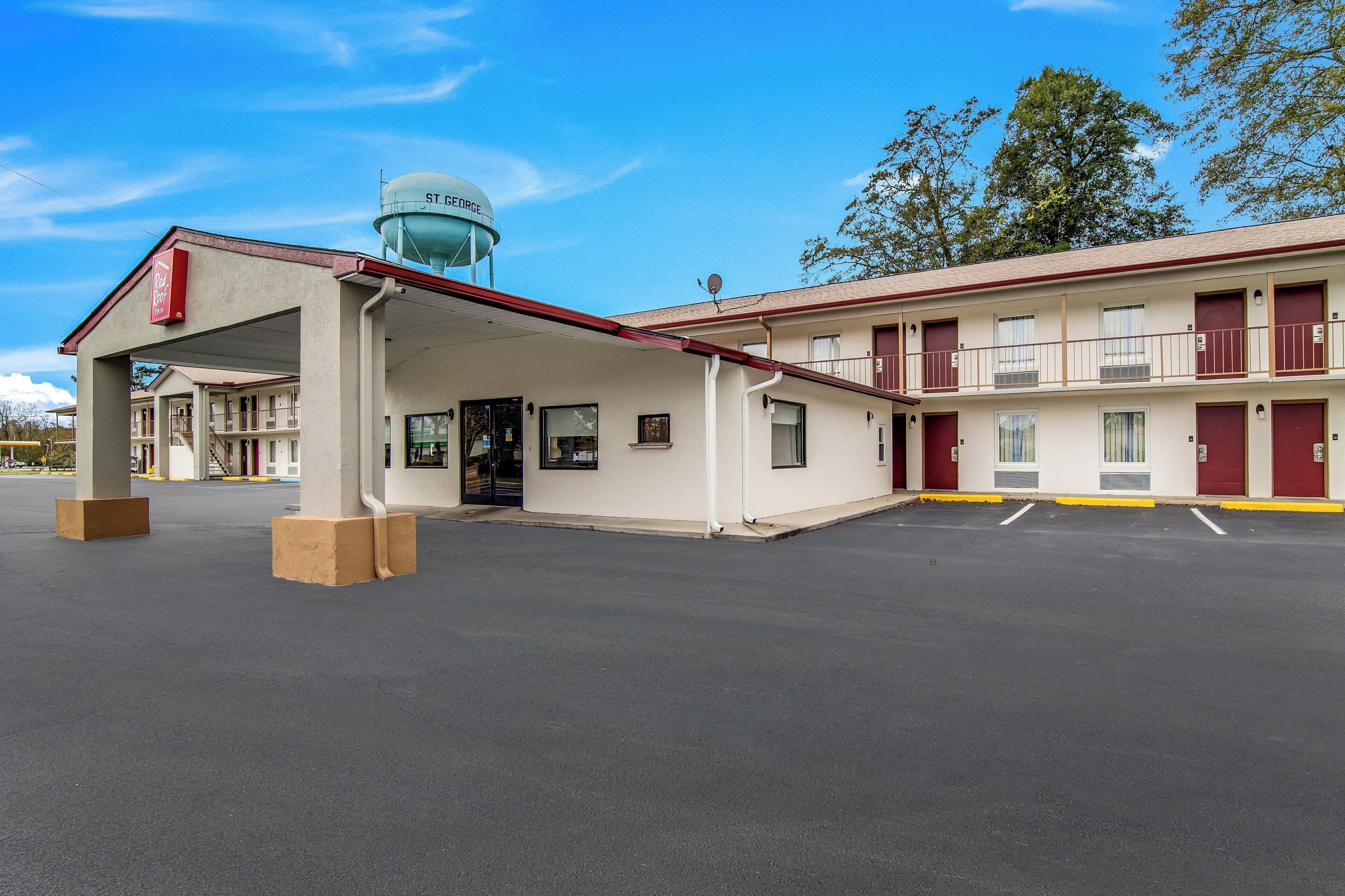 A motel with a covered parking area, a water tower, and a two-story building with multiple rooms.