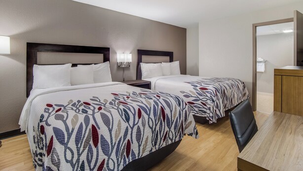 A hotel room with two beds, a wooden desk, and a mirror. - Red Roof Inn St George, SC (St. George)