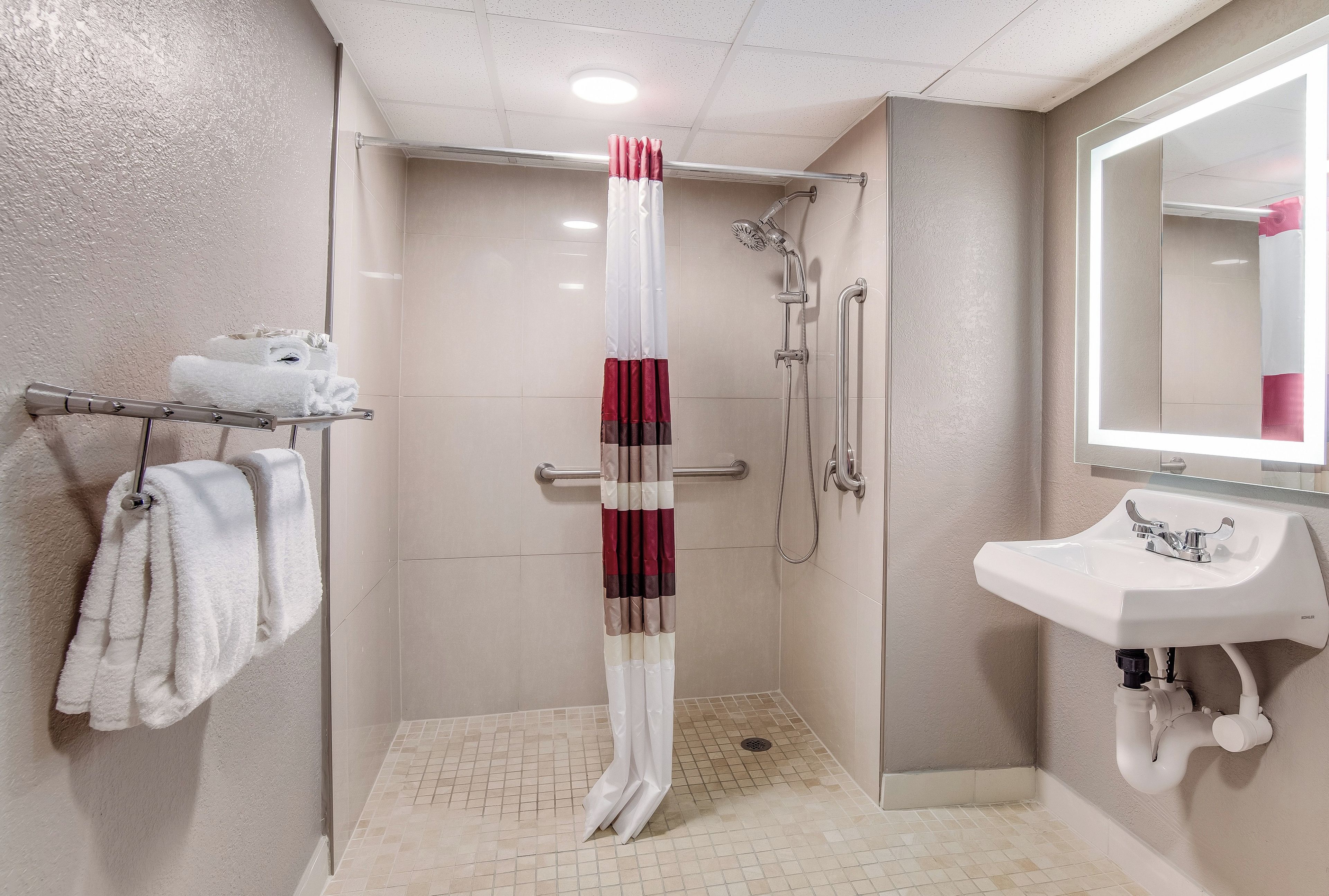 A bathroom with a shower, a towel rack with towels, and a sink with a mirror.