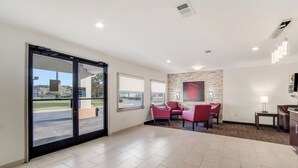 A hotel lobby with a large sliding glass door, a reception desk, a seating area with red chairs, and a stone accent wall. - Red Roof Inn St George, SC (St. George)