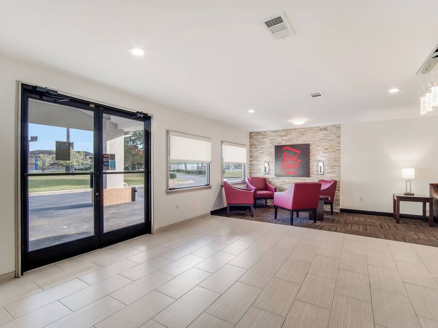 A hotel lobby with a large sliding glass door, a reception desk, a seating area with red chairs, and a stone accent wall.
