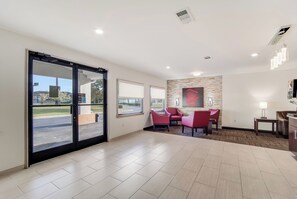 A hotel lobby with a large sliding glass door, a reception desk, a seating area with red chairs, and a stone accent wall. - Red Roof Inn St George, SC (St. George)