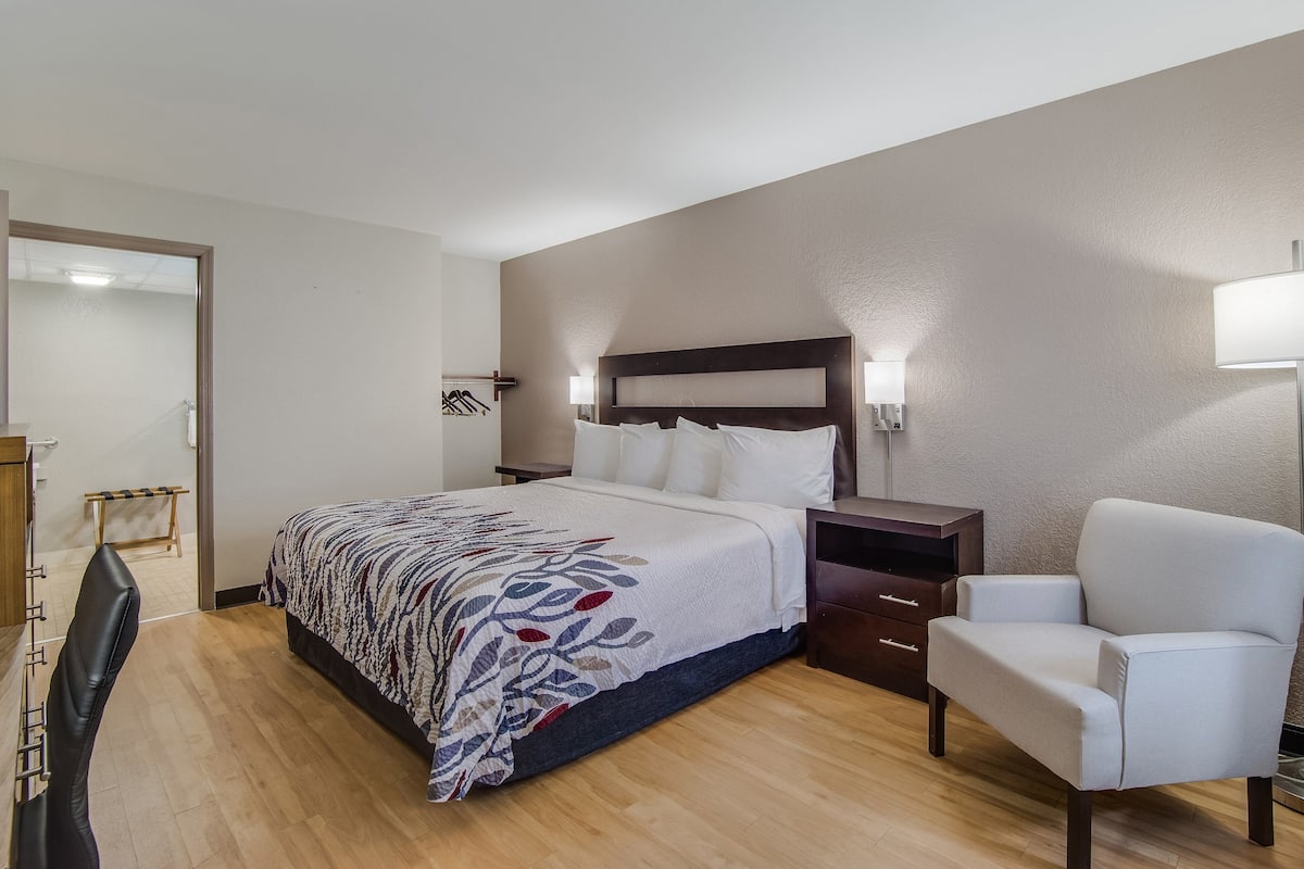 Une chambre d’hôtel avec un lit, une chaise, une table de chevet et une armoire.