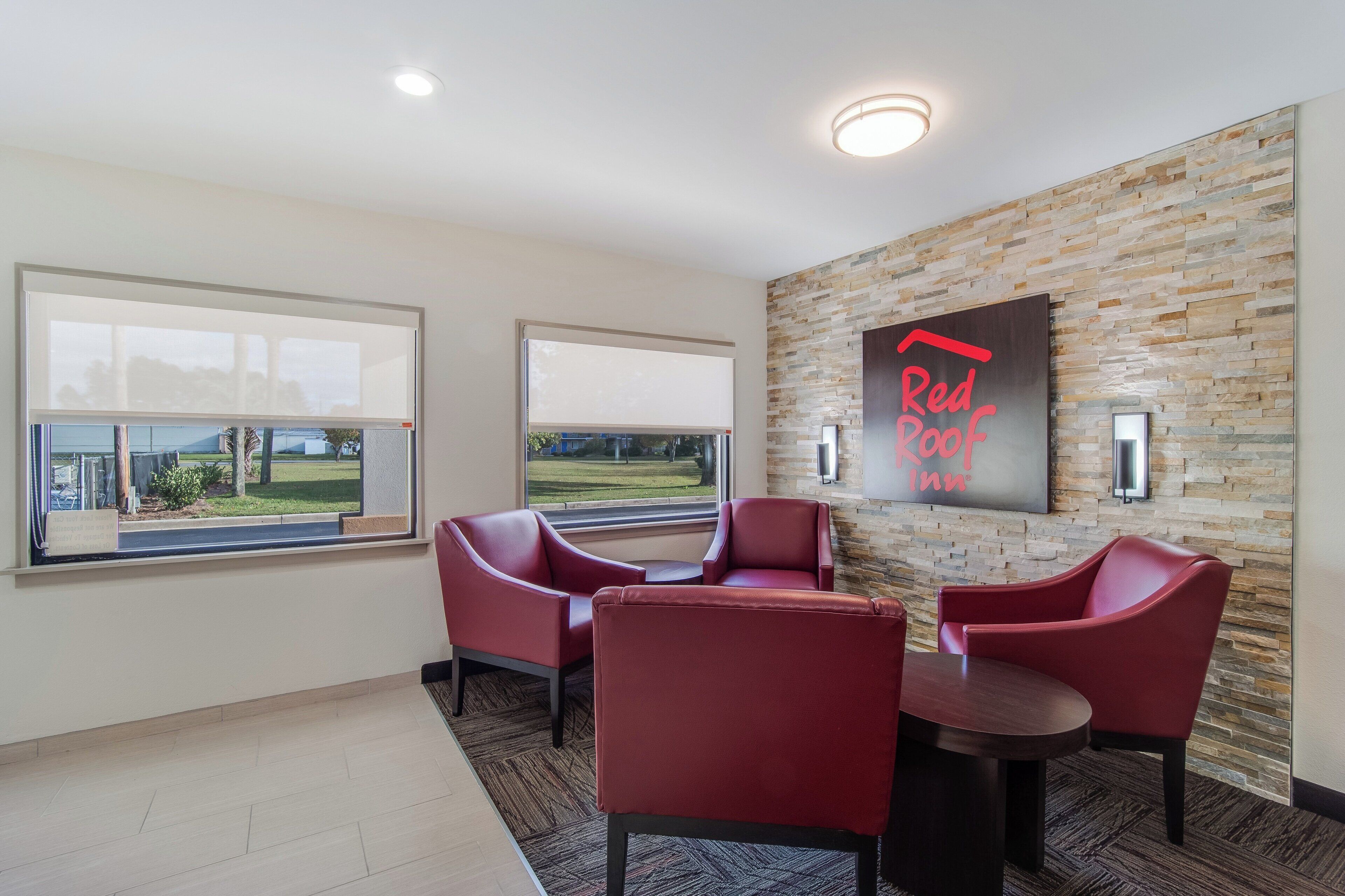 A hotel lobby with two red leather chairs, a small table, a Red Roof Inn sign, and a stone wall.