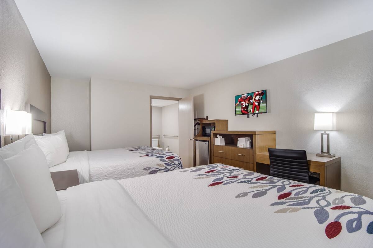 Ein Hotelzimmer mit zwei Betten, einem Schreibtisch, einem Sessel, einem Fernseher und einem Badezimmer.