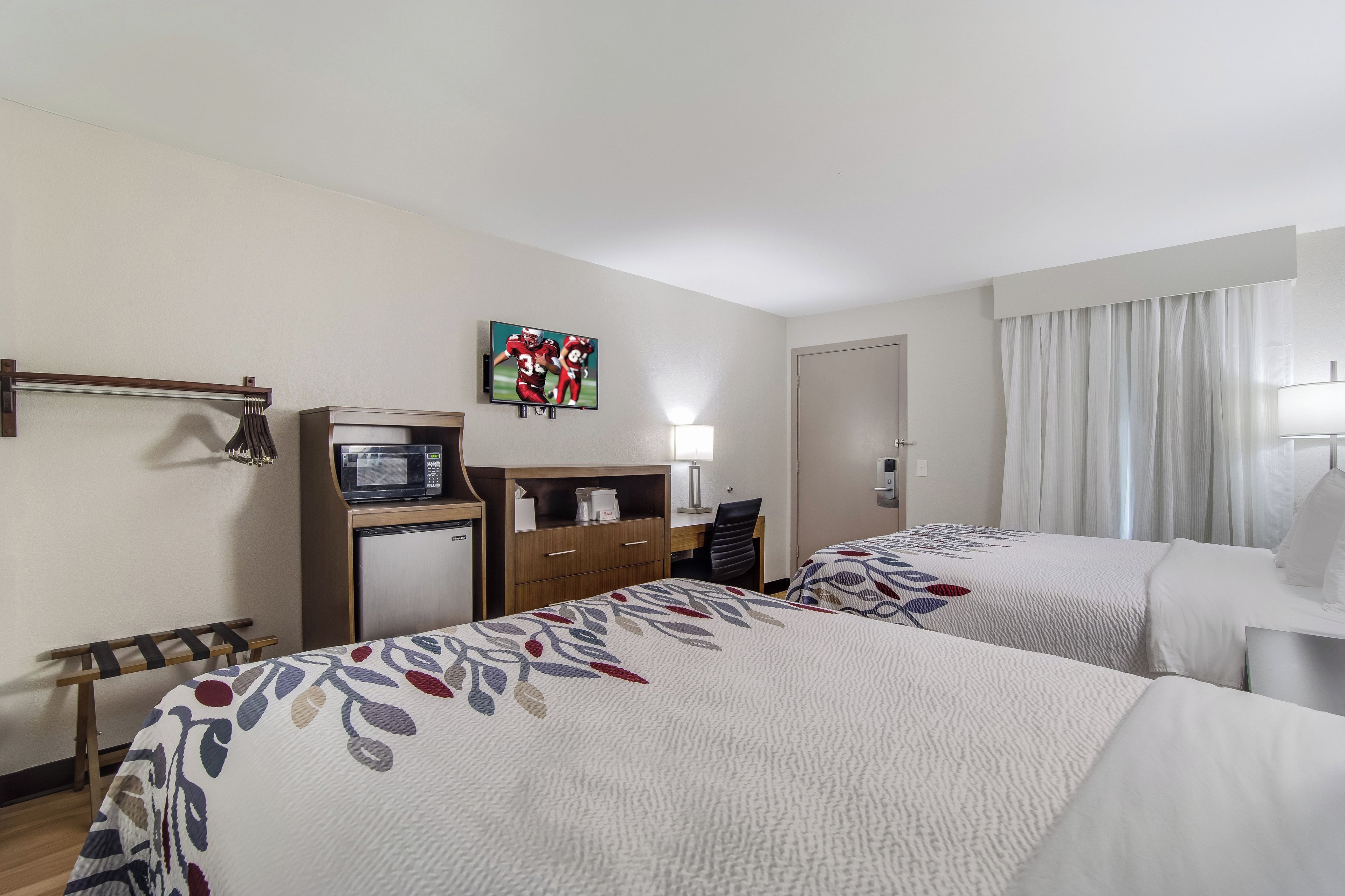 A hotel room with two beds, a desk with a computer, a TV mounted on the wall, and a minibar.