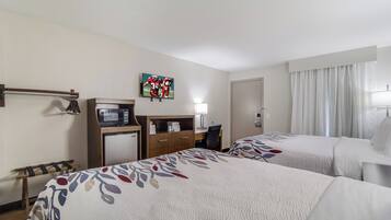 A hotel room with two beds, a desk with a computer, a TV mounted on the wall, and a minibar.