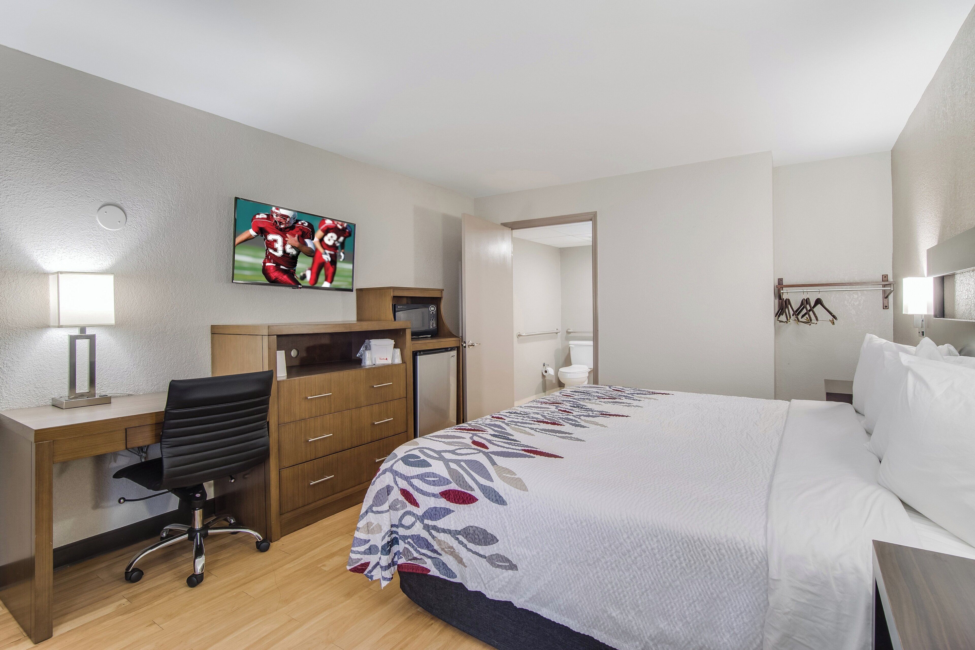 Habitación de hotel con cama, escritorio con silla, televisión y baño visible a través de una puerta abierta.