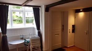 Una habitación con ventana, radiador, una mesa con sillas y una puerta.