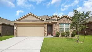 A single-story house with a beige garage door, a brick facade, and a small front yard with a tree and shrubs.