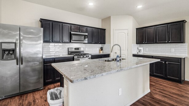 A modern kitchen with dark cabinets, stainless steel appliances, and a granite countertop island.