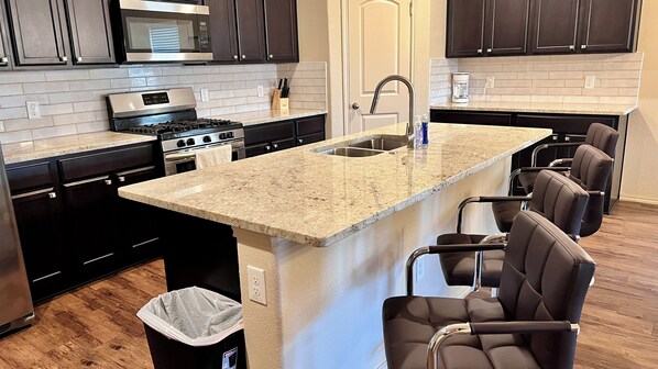 A modern kitchen with dark cabinetry, a granite countertop, stainless steel appliances, and a built-in island with bar seating.