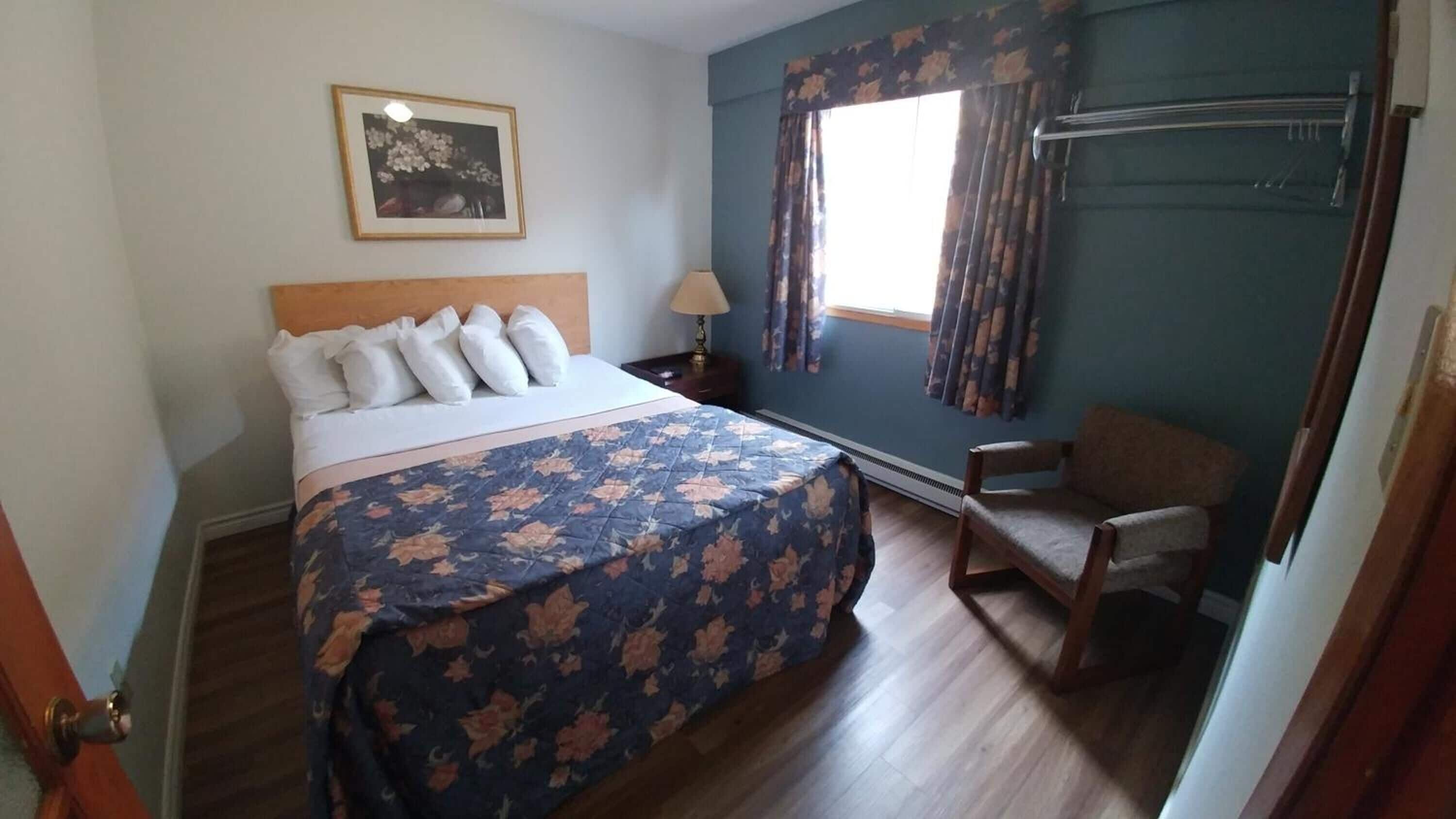 A bedroom with a bed, a chair, a window with curtains, a picture on the wall, and a heater.