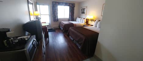A hotel room with a bed, a desk with a computer, a coffee maker, and a window with curtains.