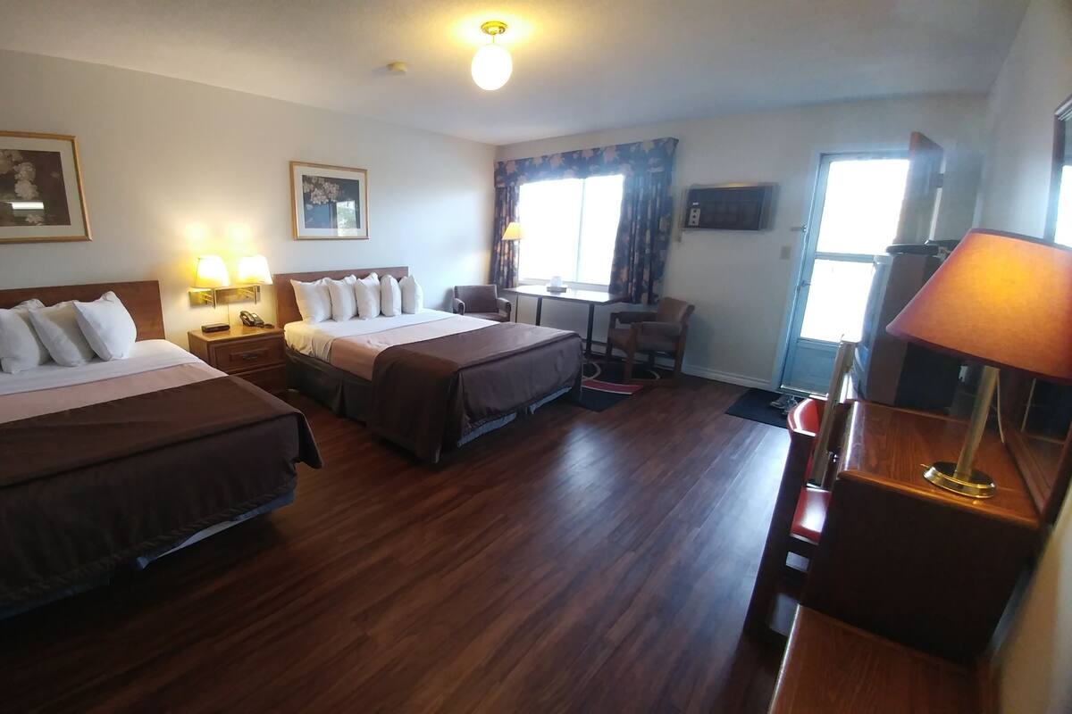 A hotel room with two beds, a desk, a chair, a lamp, and a window with curtains.