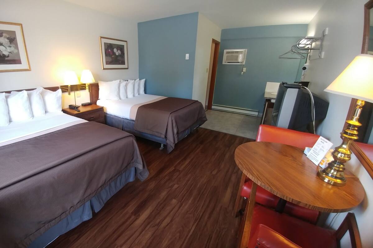 A hotel room with two beds, a wooden floor, a small table with a lamp, and a chair.