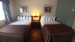 A hotel room with two beds, each with white bedding and brown headboards. There are two wall-mounted lamps on a wooden nightstand between the beds.